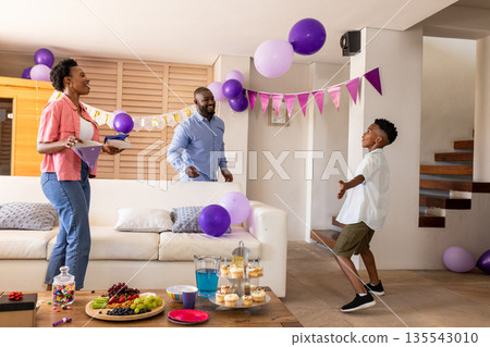 Family celebrating birthday at home, smiling and playing with purple balloons Family celebrating birthday at home, smiling and playing with purple balloons 135543010