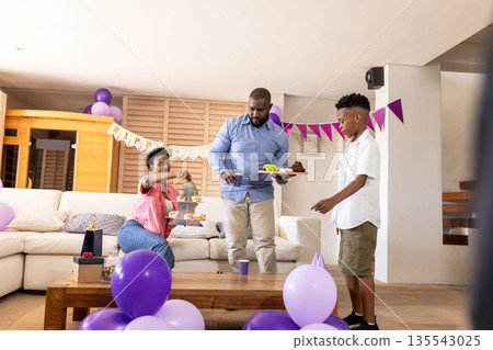 Family celebrating birthday at home, decorating with balloons and serving snacks Family celebrating birthday at home, decorating with balloons and serving snacks 135543025