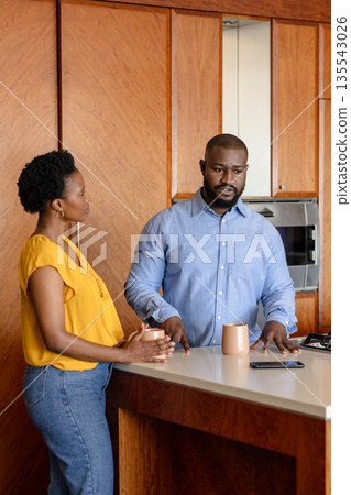 Couple in kitchen discussing plans while holding coffee mugs, looking focused 135543026