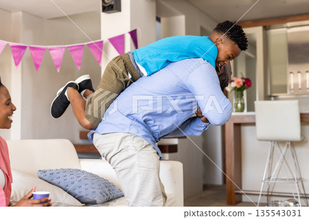 Father playing with son on back in living room, mother smiling nearby Father playing with son on back in living room, mother smiling nearby 135543031