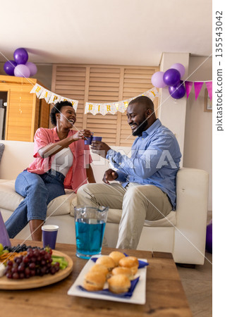 Celebrating at home, joyful couple toasting with drinks on cozy sofa Celebrating at home, joyful couple toasting with drinks on cozy sofa 135543042