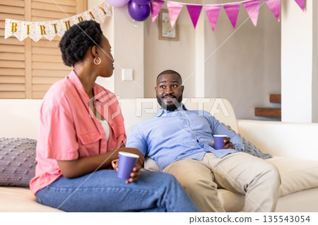 Celebrating birthday at home, couple enjoying conversation with drinks on sofa Celebrating birthday at home, couple enjoying conversation with drinks on sofa 135543054