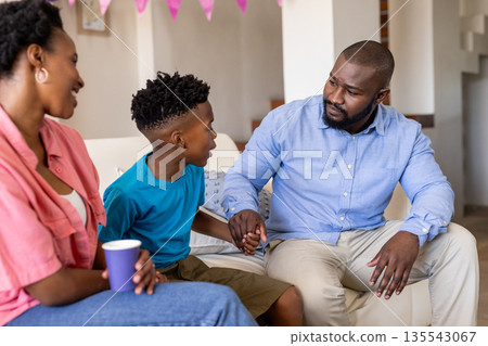 Father and son having heartfelt conversation at home, mother smiling nearby Father and son having heartfelt conversation at home, mother smiling nearby 135543067