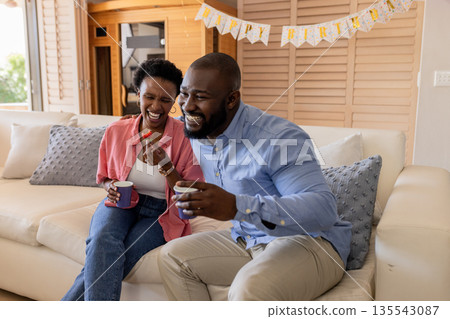 Celebrating birthday, happy couple enjoying coffee and laughter on cozy sofa Celebrating birthday, happy couple enjoying coffee and laughter on cozy sofa 135543087
