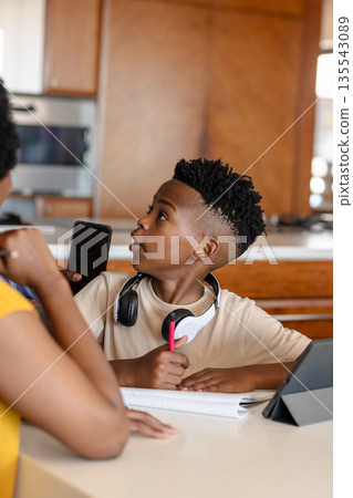 Boy at home holding smartphone and pen, looking up from homework Boy at home holding smartphone and pen, looking up from homework 135543089