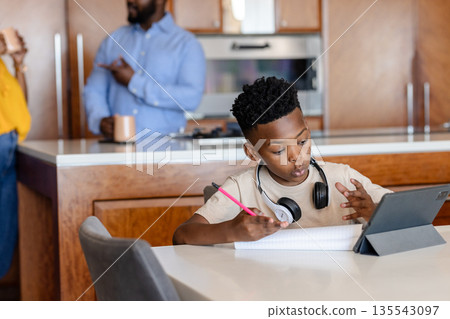 Young boy using tablet and writing in notebook at home, focused on learning Young boy using tablet and writing in notebook at home, focused on learning 135543097