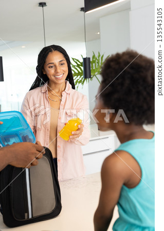 Mother packing lunchbox and juice for daughter at home, smiling warmly Mother packing lunchbox and juice for daughter at home, smiling warmly 135543105