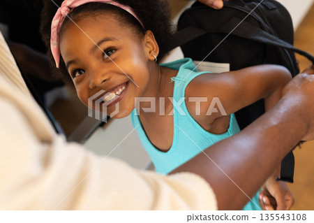 Smiling girl wearing backpack, getting ready for school with parent's help 135543108