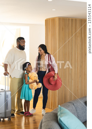 Family arriving at hotel, smiling and carrying luggage and teddy bear 135543114