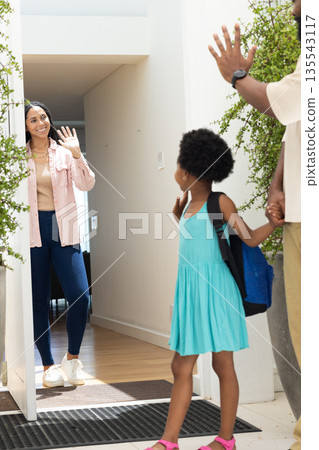 Family greeting at doorway, young girl with backpack waving and smiling warmly Family greeting at doorway, young girl with backpack waving and smiling warmly 135543117