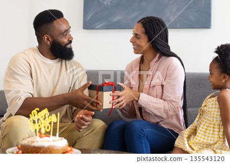 Family exchanging gift at home, smiling and celebrating birthday with cake 135543120