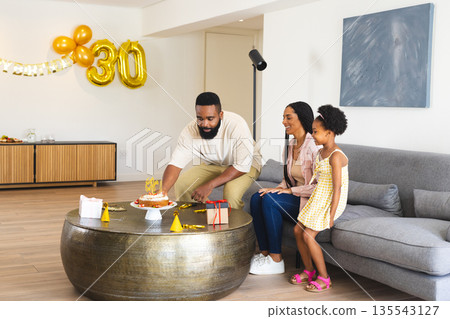 Celebrating birthday at home, family enjoying cake and gifts together on sofa 135543127