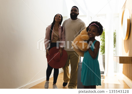 Family arriving at home, smiling and carrying suitcase and teddy bear Family arriving at home, smiling and carrying suitcase and teddy bear 135543128