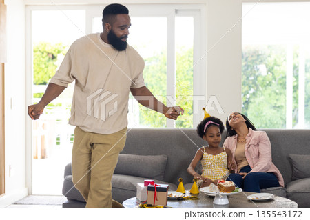 Father dancing while daughter and mother enjoy birthday cake at home Father dancing while daughter and mother enjoy birthday cake at home 135543172