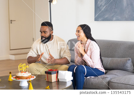 Celebrating birthday, couple sitting on couch with cake and gift boxes 135543175