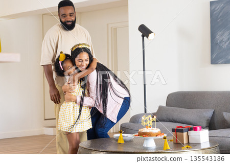 Celebrating birthday, happy family hugging near cake and gifts in living room Celebrating birthday, happy family hugging near cake and gifts in living room 135543186
