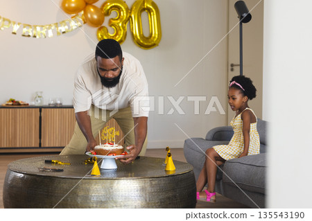 Father placing birthday cake on table while child watching in living room celebration Father placing birthday cake on table while child watching in living room celebration 135543190