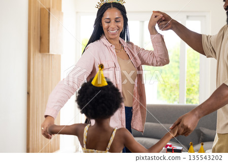 Celebrating at home, joyful family dancing together wearing party hats Celebrating at home, joyful family dancing together wearing party hats 135543202