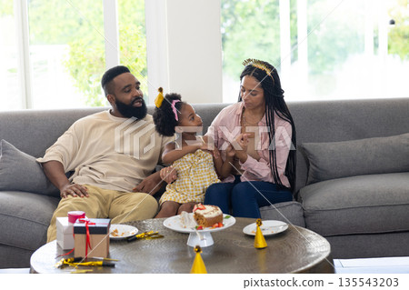 Family celebrating birthday at home, parents and daughter enjoying cake on sofa Family celebrating birthday at home, parents and daughter enjoying cake on sofa 135543203