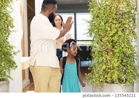 Father waving goodbye as daughter with backpack leaving for school, mother watching 135543211