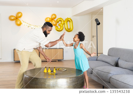 Father and daughter celebrating birthday at home, giving high five with joy 135543238