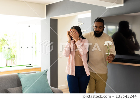 Man surprising woman with flowers at home, creating joyful moment together Man surprising woman with flowers at home, creating joyful moment together 135543244