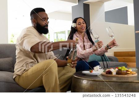 Couple enjoying wine and snacks at home, sharing joyful moments together Couple enjoying wine and snacks at home, sharing joyful moments together 135543248