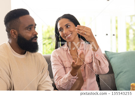 Smiling woman showing necklace to man on sofa at home, enjoying conversation Smiling woman showing necklace to man on sofa at home, enjoying conversation 135543255