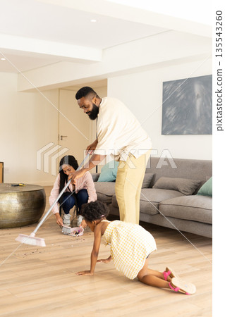 Family cleaning living room together, father sweeping while mother and child help 135543260