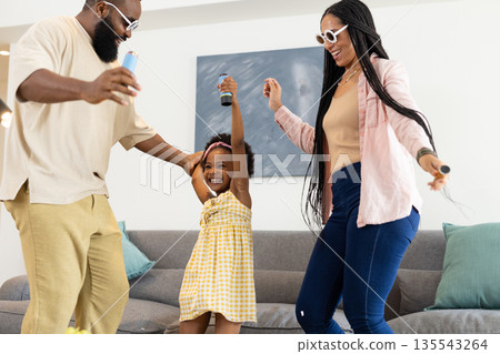African American family dancing joyfully at home, holding microphones and smiling African American family dancing joyfully at home, holding microphones and smiling 135543264