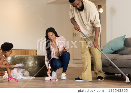 Family cleaning living room together, sweeping and picking up trash with dustpan 135543265