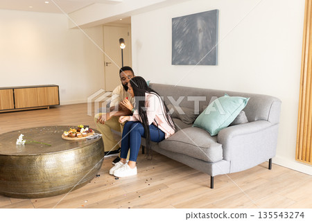 Couple sitting on sofa at home, enjoying sweet treats and sharing moment 135543274