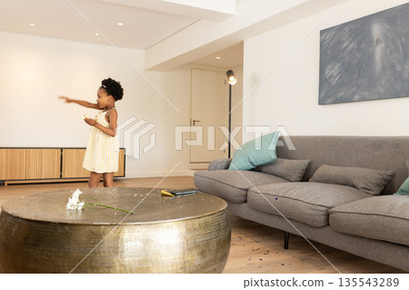 At home, African American child in yellow dress holding snack, looking curious At home, African American child in yellow dress holding snack, looking curious 135543289