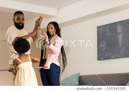 Dancing playfully at home, African American family smiling and laughing together Dancing playfully at home, African American family smiling and laughing together 135543295