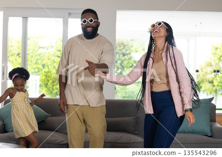 Family enjoying playful dance together at home, wearing fun sunglasses and smiling 135543296