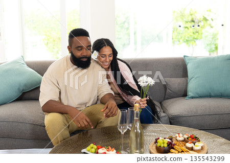 Couple relaxing on sofa, enjoying snacks and flowers in cozy living room 135543299