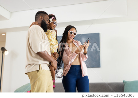 Family enjoying time together at home, smiling and looking at smartphone Family enjoying time together at home, smiling and looking at smartphone 135543303