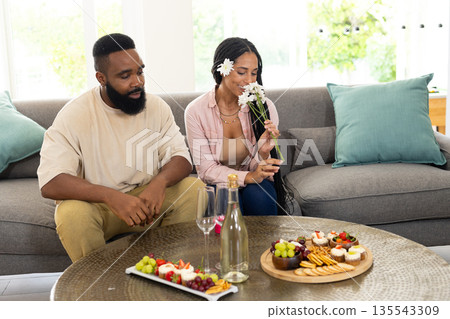 At home, African American couple with snacks and flowers, feeling relaxed together At home, African American couple with snacks and flowers, feeling relaxed together 135543309