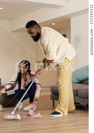 Man sweeping broken glass while woman picking up pieces in living room 135543312