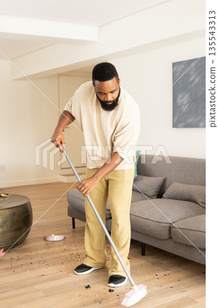 African American man sweeping floor at home, focusing on cleaning living room African American man sweeping floor at home, focusing on cleaning living room 135543313