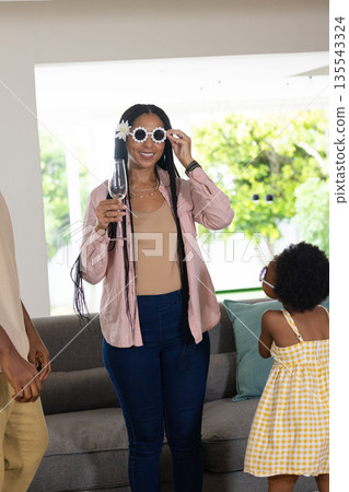 Woman wearing flower sunglasses holding drink, smiling with child in yellow dress 135543324