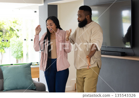 African American couple joyfully dancing together at home in living room 135543326