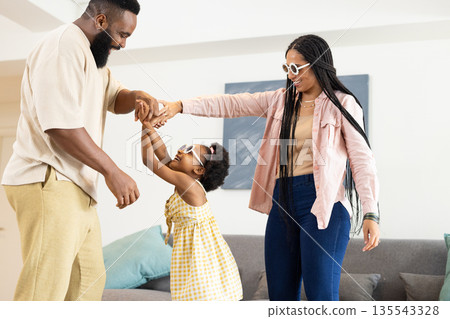 Family wearing sunglasses dancing together at home, sharing playful moments 135543328
