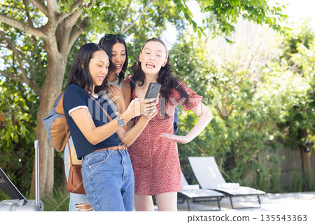 Three young women, one African American and two Caucasian, laughing while looking at smartphone outd Three young women, one African American and two Caucasian, laughing while looking at smartphone outd 135543363