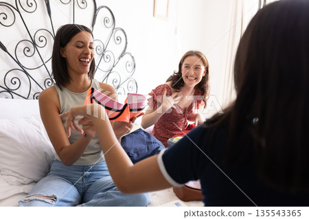 Laughing together on bed, three young women share joyful moment indoors 135543365