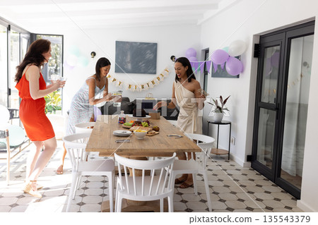 Setting up festive table, three women in colorful dresses prepare for celebration 135543379