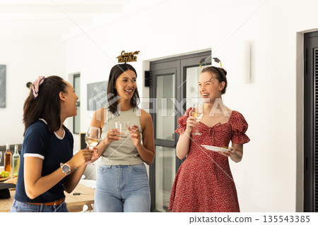 Laughing and chatting, three young women enjoy casual gathering at home 135543385