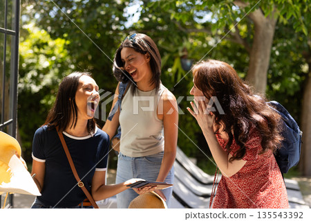 Laughing together, three young women enjoy sunny day outdoors with backpacks Laughing together, three young women enjoy sunny day outdoors with backpacks 135543392