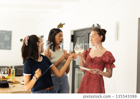 Celebrating indoors, three young women with diverse backgrounds clink glasses joyfully Celebrating indoors, three young women with diverse backgrounds clink glasses joyfully 135543399