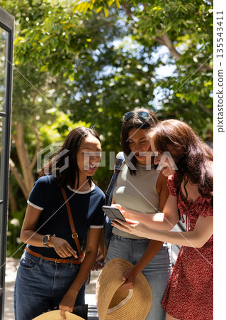 Laughing and sharing moment, three young women look at smartphone outdoors 135543411